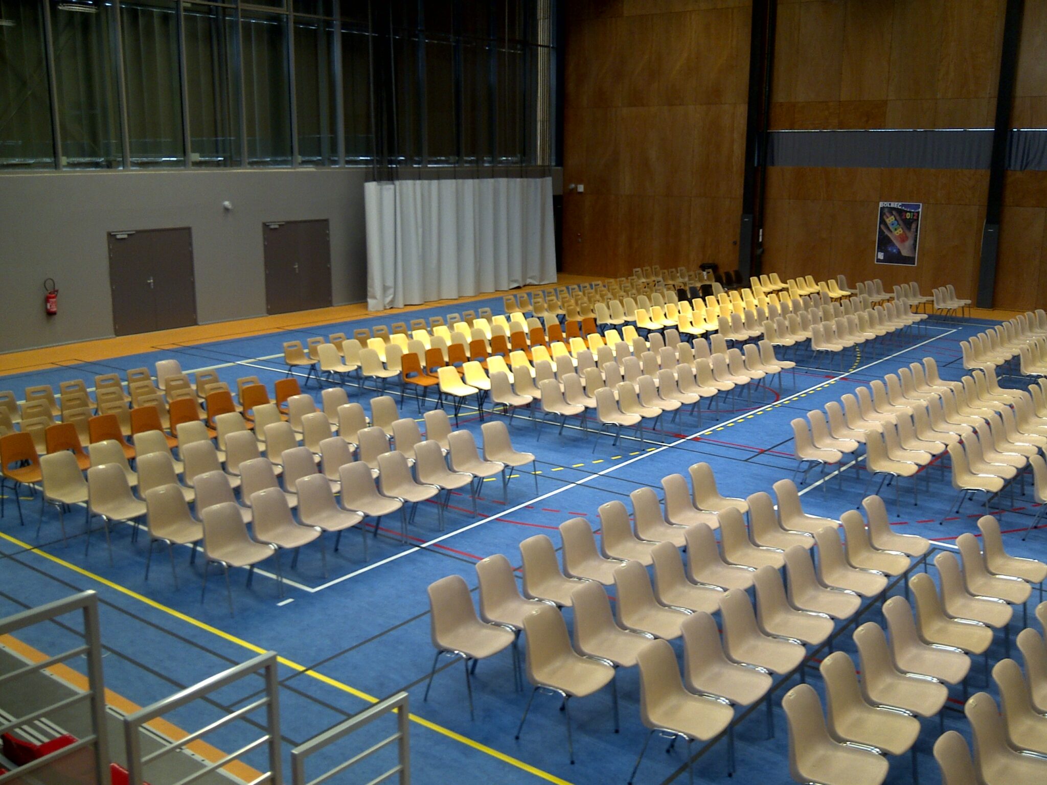 Salle polyvalente avec rangées de chaises vides.