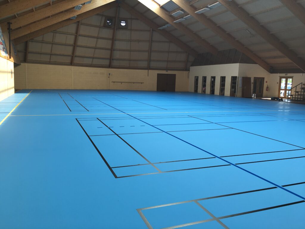 Gymnase vide avec sol bleu et lignes sportives.