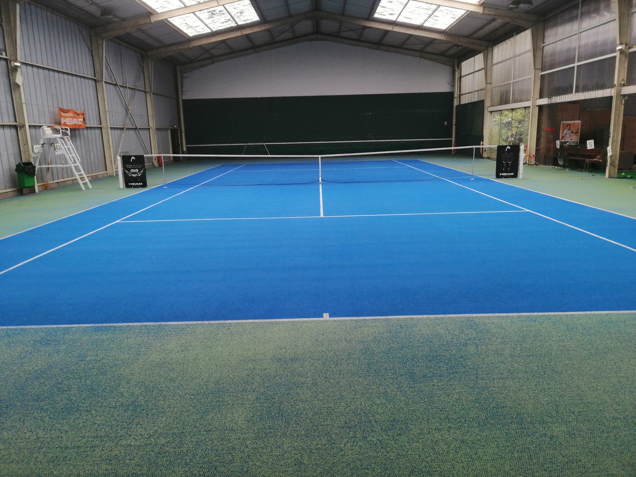 Terrain de tennis intérieur, sol bleu et vert.